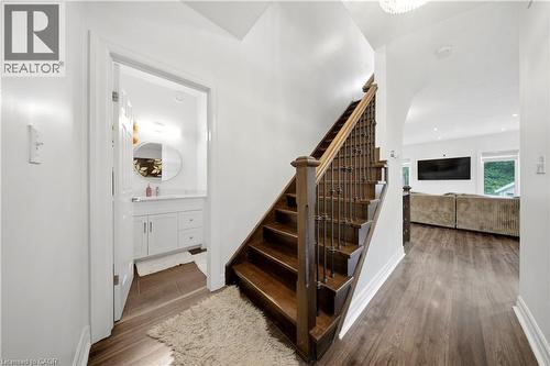 Wood-finish flooring throughout, dark wood staircase with wrought iron balusters, white vanity with integrated sink, chrome faucet, and oval mirror, and recessed lighting - 167 Broadoaks Drive, Cambridge, ON 