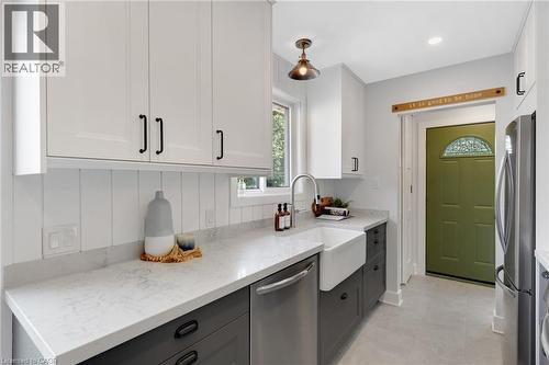 Kitchen featuring white upper cabinetry, dark lower cabinetry, light-toned countertops, a farmhouse sink with a gooseneck faucet, and a paneled backsplash - 477 Kingscourt Drive Unit# B, Waterloo, ON 