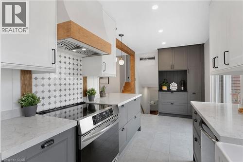 Gourmet kitchen featuring a stainless steel range, white shaker cabinetry, custom wood range hood, patterned tile backsplash, and light-colored countertops - 477 Kingscourt Drive Unit# B, Waterloo, ON 