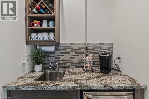 Wet bar featuring a stainless steel sink, patterned tile backsplash, granite-finish countertop, built-in wooden wine rack, and under-counter appliance - 249 Woodway Trail, Simcoe, ON 