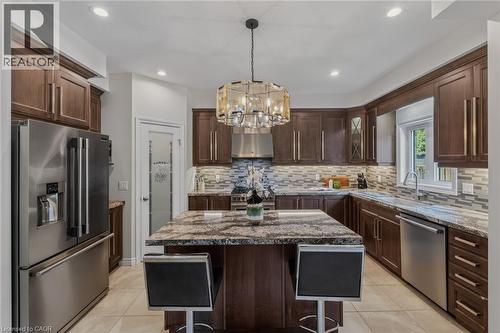 Kitchen featuring a central island with a granite countertop, dark wood-finish cabinetry, stainless steel appliances, tile flooring, and a decorative pendant light fixture - 249 Woodway Trail, Simcoe, ON 