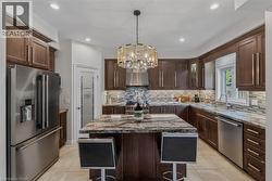 Kitchen featuring a central island with a granite countertop, dark wood-finish cabinetry, stainless steel appliances, tile flooring, and a decorative pendant light fixture - 