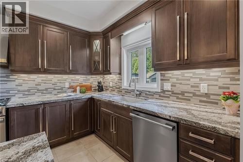 Kitchen featuring dark wood-finish cabinetry, light stone countertops, a mosaic tile backsplash, and stainless steel appliances - 249 Woodway Trail, Simcoe, ON 