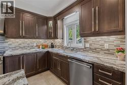Kitchen featuring dark wood-finish cabinetry, light stone countertops, a mosaic tile backsplash, and stainless steel appliances - 