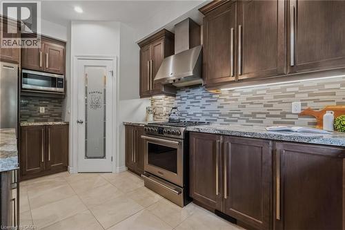 Kitchen featuring dark wood-finish cabinetry, stainless steel appliances, granite countertops, and a tiled backsplash - 249 Woodway Trail, Simcoe, ON 