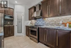 Kitchen featuring dark wood-finish cabinetry, stainless steel appliances, granite countertops, and a tiled backsplash - 