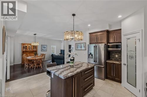 Kitchen featuring a central island with a granite countertop, dark wood-finish cabinetry, stainless steel appliances, and tile flooring - 249 Woodway Trail, Simcoe, ON 