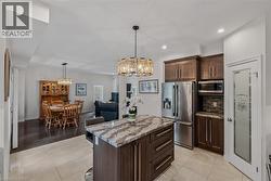 Kitchen featuring a central island with a granite countertop, dark wood-finish cabinetry, stainless steel appliances, and tile flooring - 