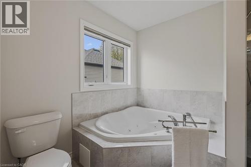 Bathroom featuring a corner jetted soaking tub with tile surround, a window with horizontal blinds, and a white toilet - 249 Woodway Trail, Simcoe, ON 