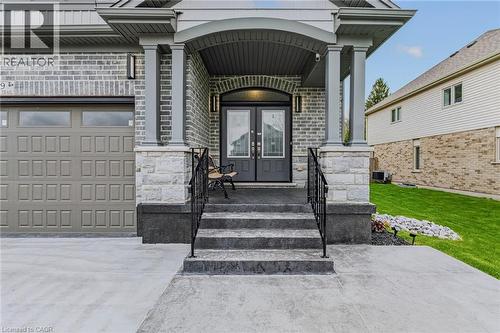 Stately brick and stone exterior featuring a covered entry, double front doors, an arched transom, and integrated exterior lighting - 249 Woodway Trail, Simcoe, ON 