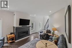 Living area featuring dark wood-finish flooring, a contemporary fireplace with dark tile surround and hearth, recessed lighting, and a staircase with dark risers and wrought iron balusters - 