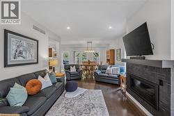 Spacious living area featuring rich wood-finish flooring, a contemporary fireplace with stacked stone surround, recessed lighting, and a broad opening to the dining area - 
