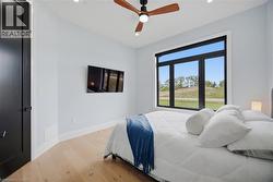 Natural wood-finish flooring, a contemporary ceiling fan, and a large multi-pane window with a roller shade - 