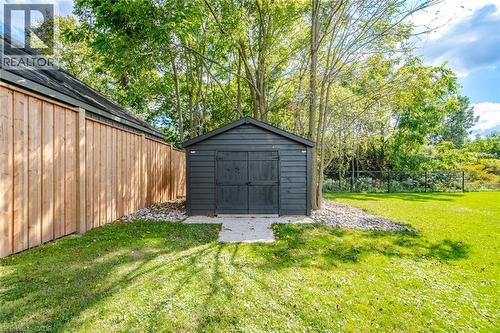 Detached black shed with concrete pad, surrounded by mature trees and a manicured lawn - 56 Augustus Street, Scotland, ON 