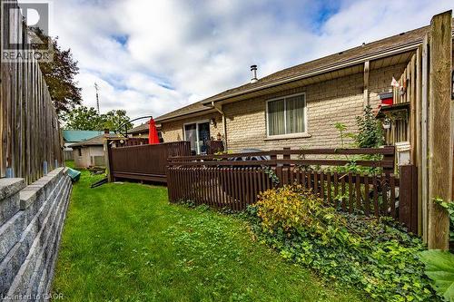 Expansive backyard featuring a manicured lawn, stone retaining wall, and a wood-finish deck with privacy fencing - 123 Mill Street, Delhi, ON 