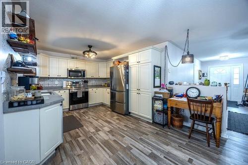 Kitchen featuring wood-finish flooring, white cabinetry, stainless steel appliances, and a tiled backsplash - 123 Mill Street, Delhi, ON 