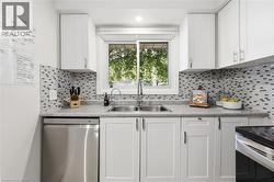 Kitchen featuring white shaker cabinetry, stainless steel dishwasher, dual basin undermount sink with gooseneck faucet, light-toned countertop, and mosaic tile backsplash - 