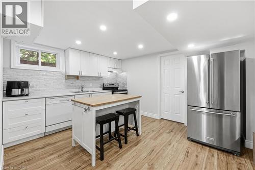 Kitchen featuring wood-finish flooring, white cabinetry, a light-toned backsplash, recessed lighting, and a stainless steel refrigerator - 312 Upper Paradise Road, Hamilton, ON 