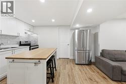 Full kitchen with white cabinetry, stainless steel appliances, wood-finish flooring, and recessed lighting - 