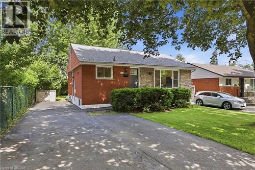 Red brick exterior with stone facade accents, mature front yard landscaping, paved driveway, and chain-link fence - 312 Upper Paradise Road, Hamilton, ON 