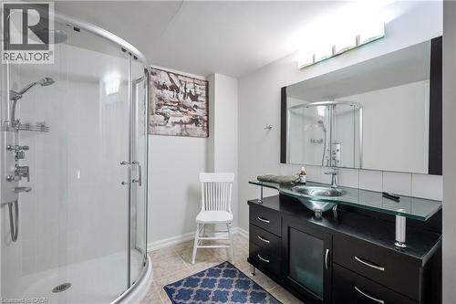 Curved glass shower enclosure with a rainfall showerhead, dark wood-finish vanity with a glass countertop, vessel sink, and a large wall-mounted mirror with integrated lighting - 12 Langevin Drive, Wasaga Beach, ON 