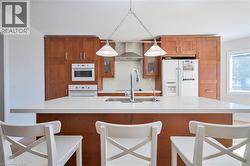 Kitchen featuring a central island with a sink and faucet, white countertops, wood cabinetry, and integrated appliances - 