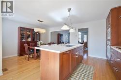 Kitchen featuring a central island with an undermount sink, light-toned wood-finish flooring, integrated wall ovens, and recessed lighting - 