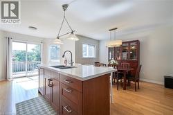 Central kitchen island with an undermount double sink, a white countertop, and wood-finish cabinetry featuring stainless steel hardware - 