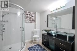 Curved glass shower enclosure with a rainfall showerhead, dark wood-finish vanity with a glass countertop, vessel sink, and a large wall-mounted mirror with integrated lighting - 