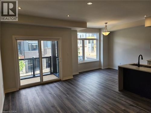 Spacious living area featuring wood-finish flooring, recessed lighting, and a sliding glass door opening to a private balcony with black metal railings - 155 Equestrian Way Unit# 152, Cambridge, ON 