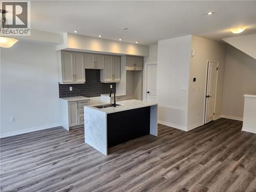 Contemporary kitchen island with a stone finish countertop and integrated sink, recessed lighting, wood-finish flooring, light cabinetry, and dark subway tile backsplash - 155 Equestrian Way Unit# 152, Cambridge, ON 