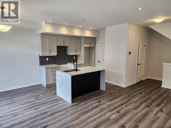 Contemporary kitchen island with a stone finish countertop and integrated sink, recessed lighting, wood-finish flooring, light cabinetry, and dark subway tile backsplash - 