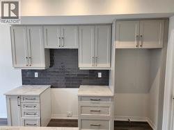 White shaker-style cabinetry, white countertops with subtle veining, dark subway tile backsplash, and dark wood-finish flooring - 
