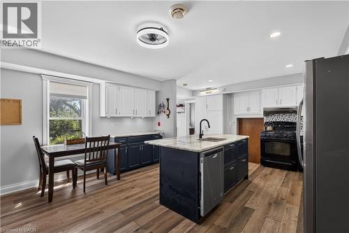 Open-concept kitchen featuring an island with a built-in sink and dishwasher, wood-finish flooring, two-tone cabinetry with white upper and dark lower units, recessed lighting, and a window providing - 42841 Highway 3, Wainfleet, ON 
