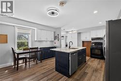 Open-concept kitchen featuring an island with a built-in sink and dishwasher, wood-finish flooring, two-tone cabinetry with white upper and dark lower units, recessed lighting, and a window providing - 