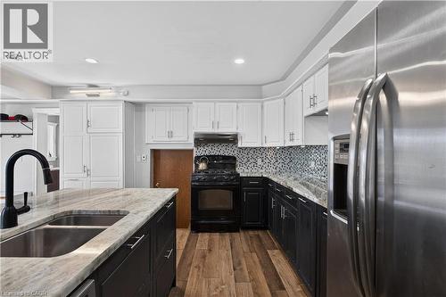 Kitchen featuring an island with a double basin sink and black faucet, wood-finish flooring, two-tone cabinetry, a tile backsplash, and stainless steel appliances - 42841 Highway 3, Wainfleet, ON 