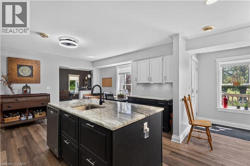 Kitchen featuring a central island with a granite-style countertop and undermount sink, dark cabinetry with chrome hardware, wood-finish flooring, and recessed lighting - 42841 Highway 3, Wainfleet, ON 