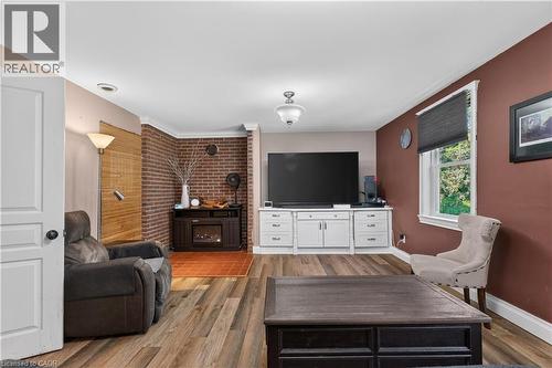 Living area featuring wood-finish flooring, a wall-mounted entertainment center with white cabinetry, a brick accent wall, and an electric fireplace with a dark wood surround - 42841 Highway 3, Wainfleet, ON 