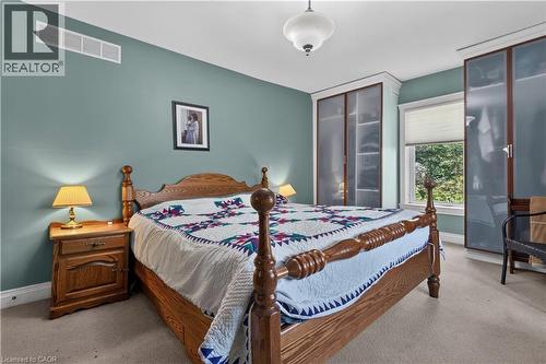 Bedroom featuring built-in cabinetry with frosted glass doors, a single window with blinds, and light carpet flooring - 42841 Highway 3, Wainfleet, ON 