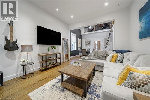 Recessed lighting illuminates the living space, featuring wood-finish flooring and a partial loft with a black railing - 28 Cambridge Street, Cambridge, ON 