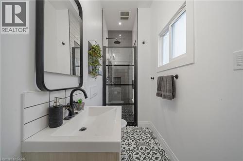 White single-basin vanity with matte black faucet, black-framed mirror, and patterned floor tile - 28 Cambridge Street, Cambridge, ON 
