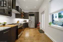 Galley kitchen with wood-finish flooring, stainless steel appliances, dark cabinetry, light countertops, and recessed lighting - 