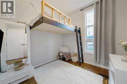 Built-in elevated bed with a ladder, wood-finish flooring, white walls, and a window with a curtain rod - 