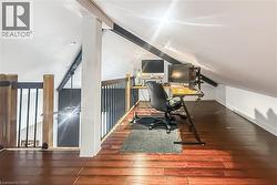 Attic loft space featuring wood-finish flooring, white vaulted ceilings, recessed lighting, and a wood and metal railing - 