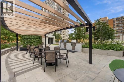 Curved wooden pergola with black metal frame, paver patio, built-in BBQ stations, and a lush green wall - 60 Central Park Roadway Unit# 2010, Etobicoke, ON 