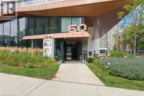 Modern building entrance with a geometric metal facade, expansive glass windows, concrete walkway, and landscaped garden beds - 60 Central Park Roadway Unit# 2010, Etobicoke, ON 
