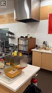 Stainless steel commercial-grade exhaust hood, white subway tile backsplash, wood-finish wall panels, light wood-finish cabinetry, dark flooring - 