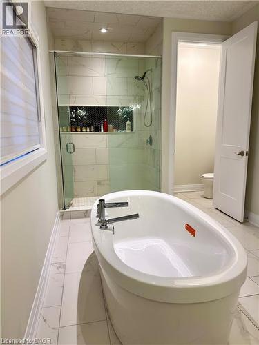 Freestanding soaking tub with polished chrome fixtures, walk-in shower with glass enclosure, tiled shower walls, and a recessed shower niche with chevron tile - 923 Eaglecrest Court, Kitchener, ON 