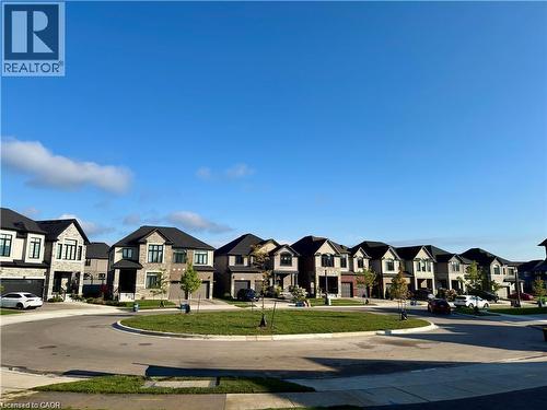 Paved circular street with a central landscaped island, surrounded by a collection of modern residences featuring stone and stucco exteriors, dark-pitched roofs, and attached garages - 923 Eaglecrest Court, Kitchener, ON 