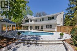 White exterior residence featuring a curved swimming pool, extensive paver patio, stone retaining wall, and a covered outdoor pavilion - 